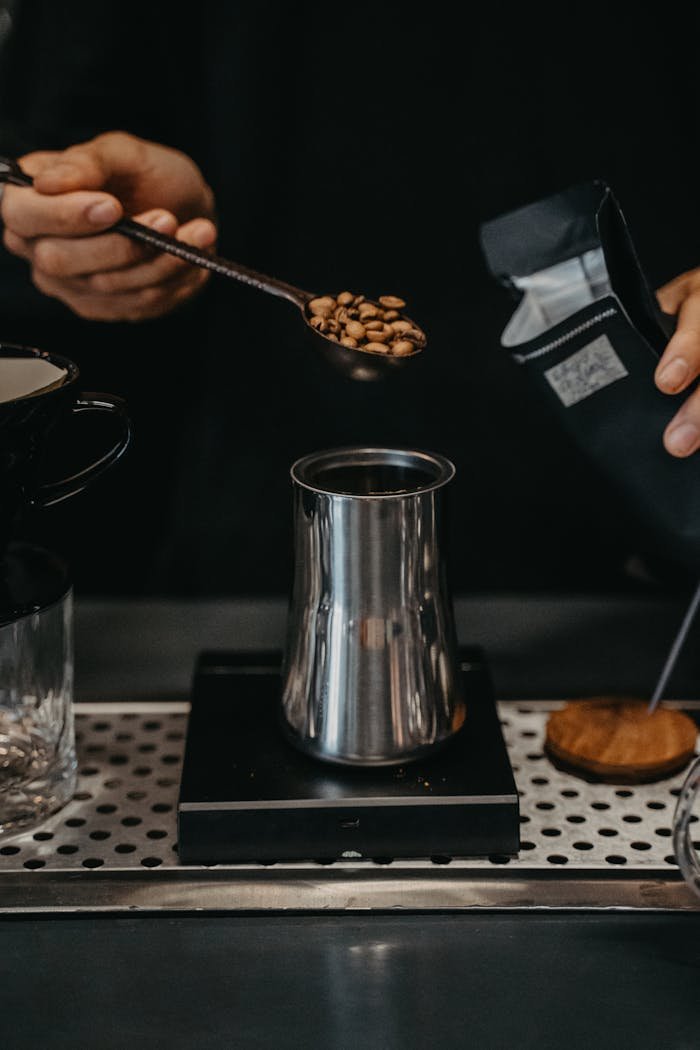 Close-up of hands making coffee with spoon and steel pot. Refined brewing method.