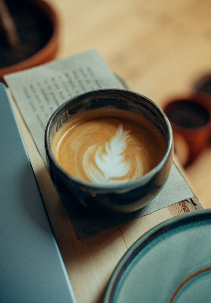 A beautifully crafted latte with latte art in a rustic ceramic cup on a wooden table.