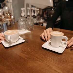 A barista serves two foamy lattes in a cozy coffee shop setting, showcasing latte art.